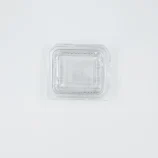 Top-down view of a clear plastic clamshell lid resting on a white surface, centered toward the bottom of the image.